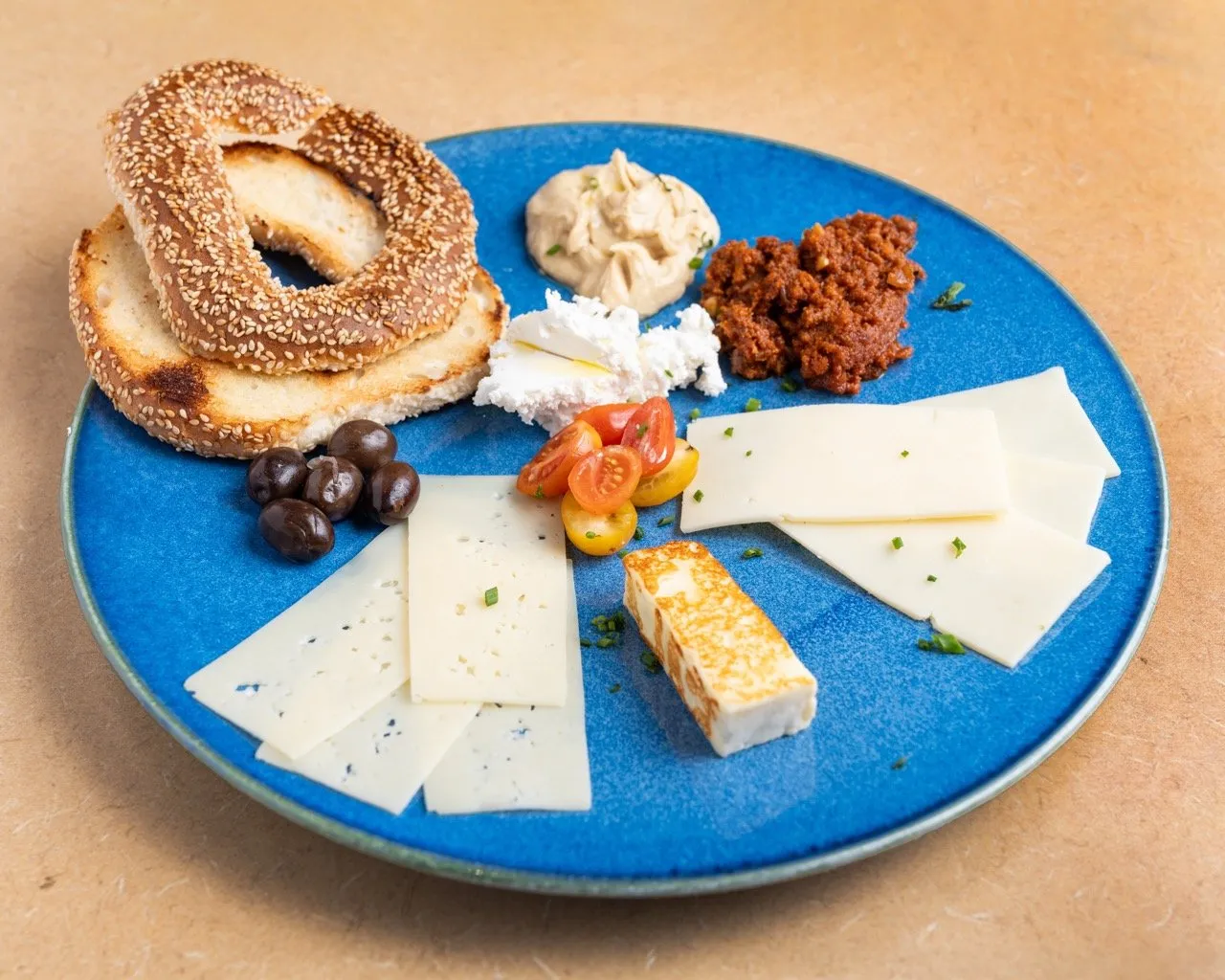 Le Plateau Déj — 4 fromages (suisse, cheddar, halloum frit, feta), olives noires, tomates cerises, mouhamara, bagel.
